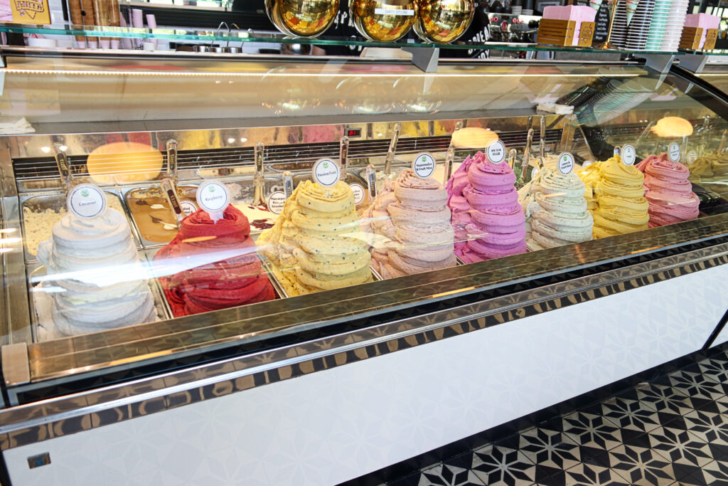 A vibrant array of gelato flavours neatly swirled in a display case, including coconut, raspberry, passionfruit, watermelon & fresh mint, dragon fruit, lemon & fresh mint, and mango