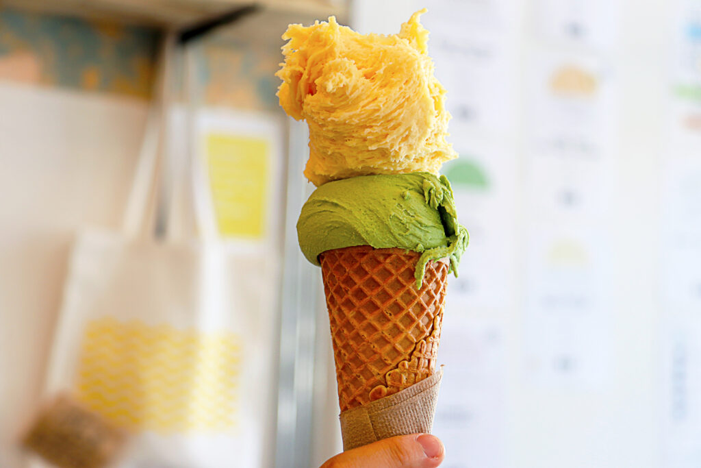 A scoop of yellow mango gelato and green matcha gelato served in a waffle cone