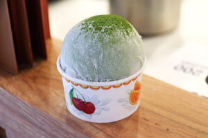 A large scoop of gelato topped with mochi (daifuku) covering a takeaway cup firmly