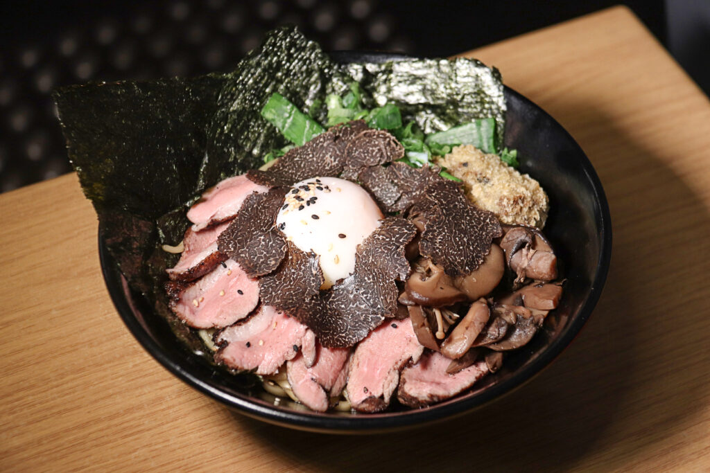 Special Truffle Duck Mazesoba with housemade noodles, duck, duck liver croquette, onsen egg, nori, shallot, mushrooms, sesame seeds and truffle slices, served in a black bowl